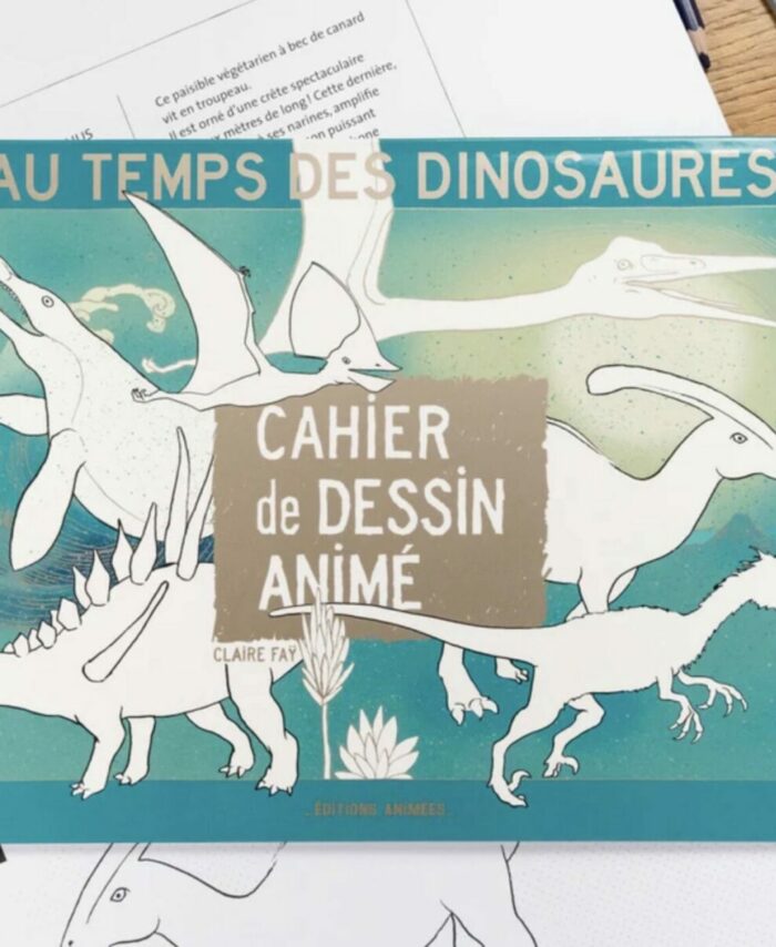 Couverture du Cahier de Dessin Animé Au Temps des Dinosaures BlinkBook posée sur un bureau avec crayons de couleur