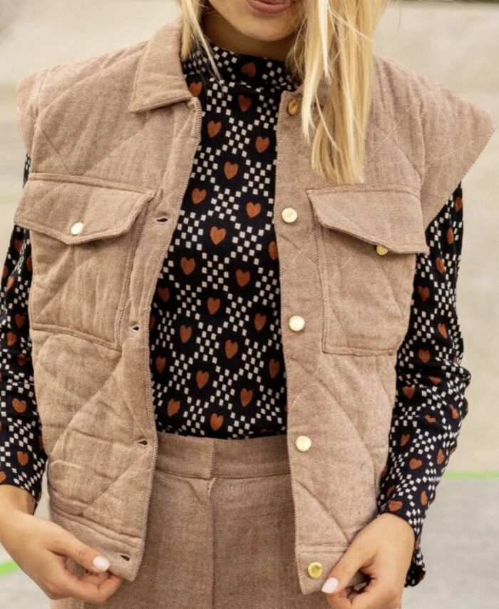 Femme portant la veste sans manches Vimil beige matelassée Apaches Collections sur une blouse à motifs.