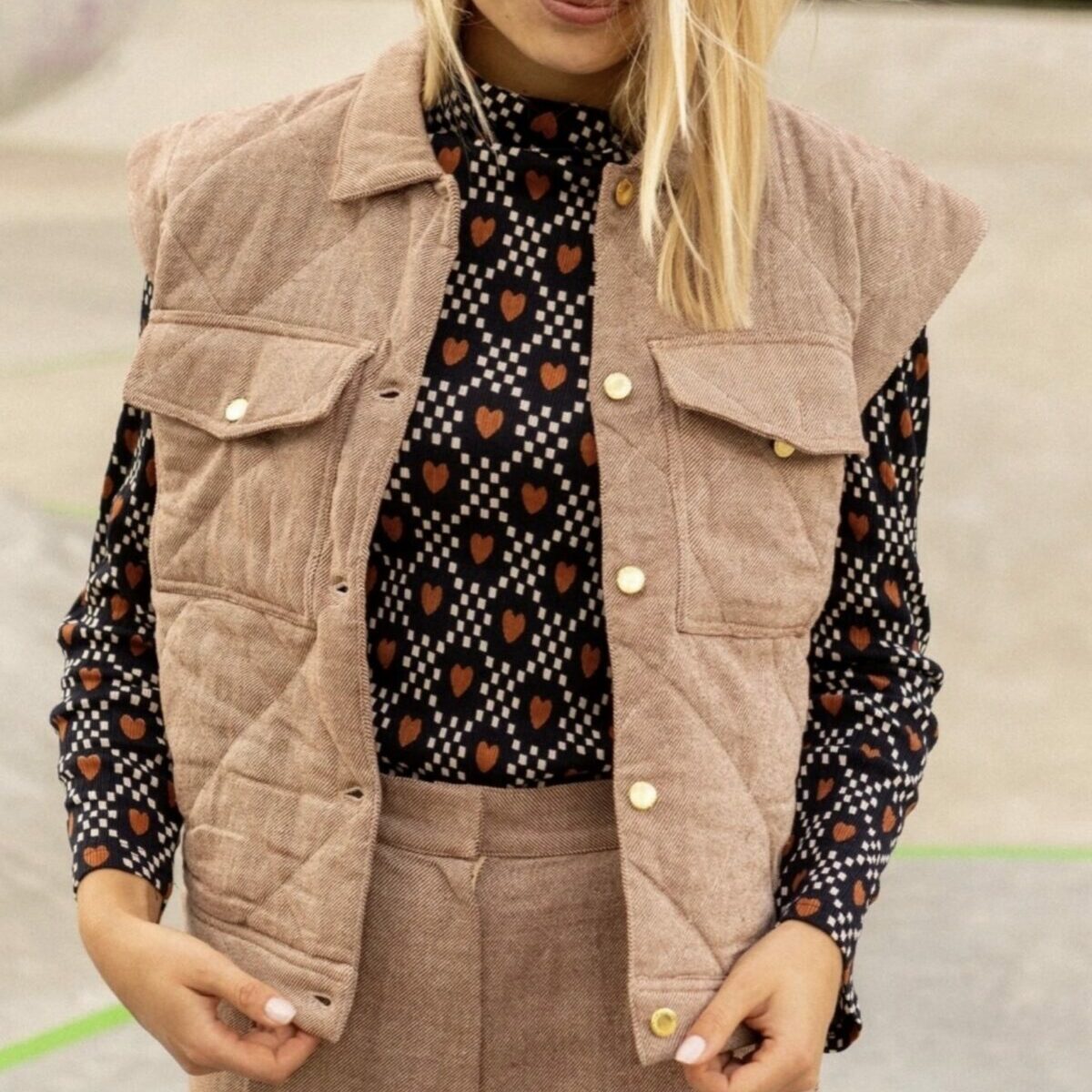 Femme portant la veste sans manches Vimil beige matelassée Apaches Collections sur une blouse à motifs.