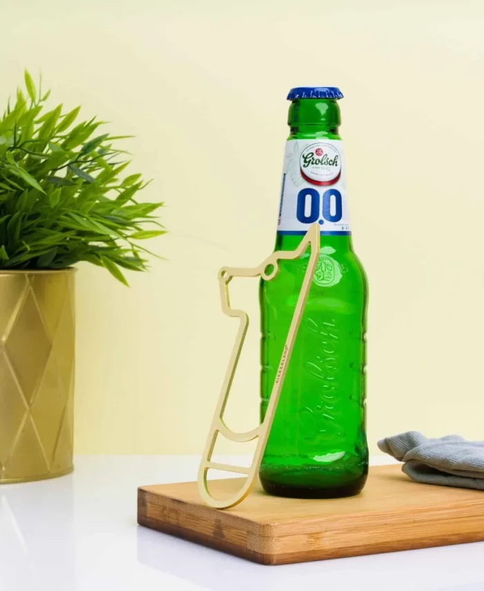 Gros plan sur une main utilisant le décapsuleur doré en forme de chien pour ouvrir une bouteille de bière.