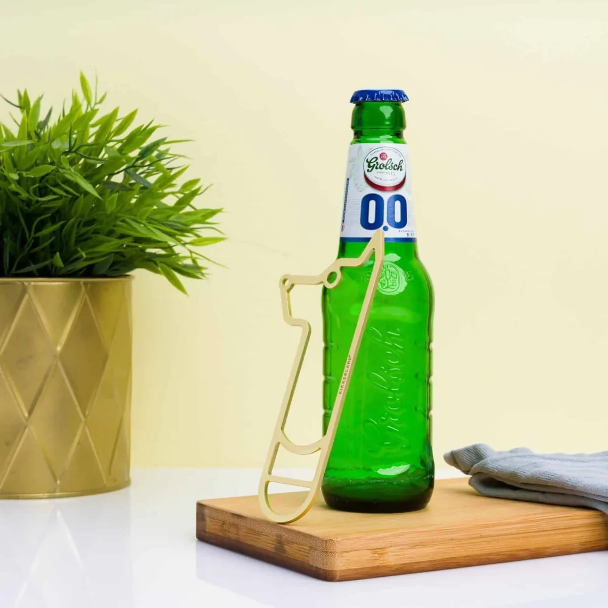 Gros plan sur une main utilisant le décapsuleur doré en forme de chien pour ouvrir une bouteille de bière.