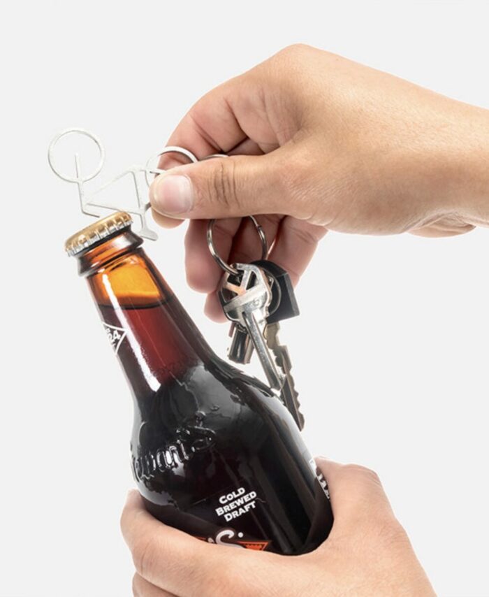 Utilisation du porte-clés décapsuleur en forme de vélo Kikkerland pour ouvrir une bouteille.