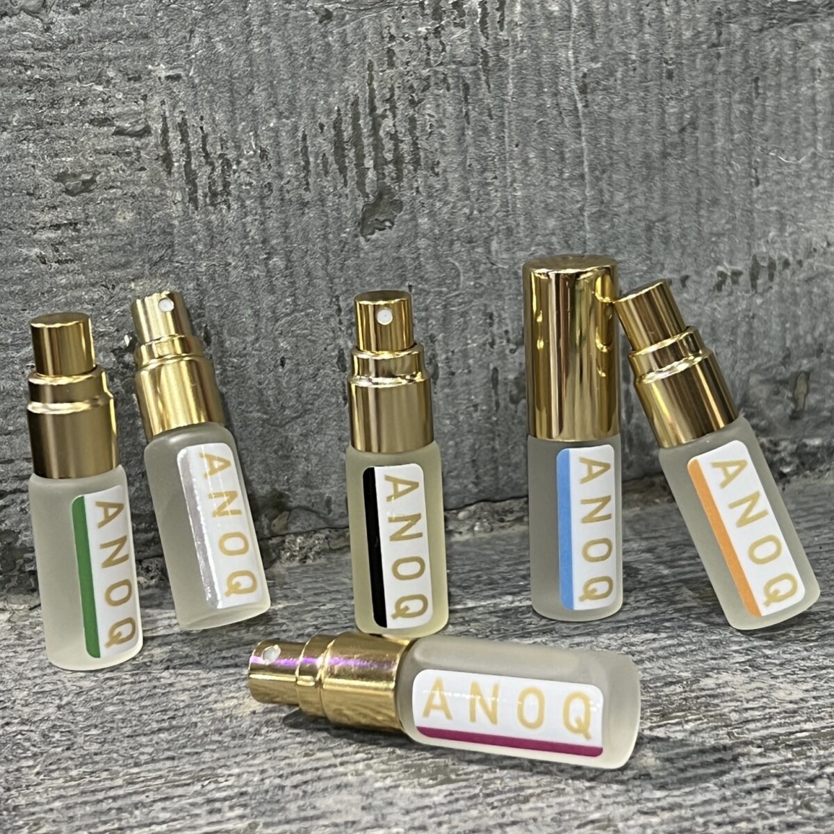 Alignement des six flacons de concentrés de parfum d'ambiance Anoq : Accord Audacieux, Ambre Noir, Mandarin des thés, Nature du Lin, Lit de Jasmin, Mystère Boisé.