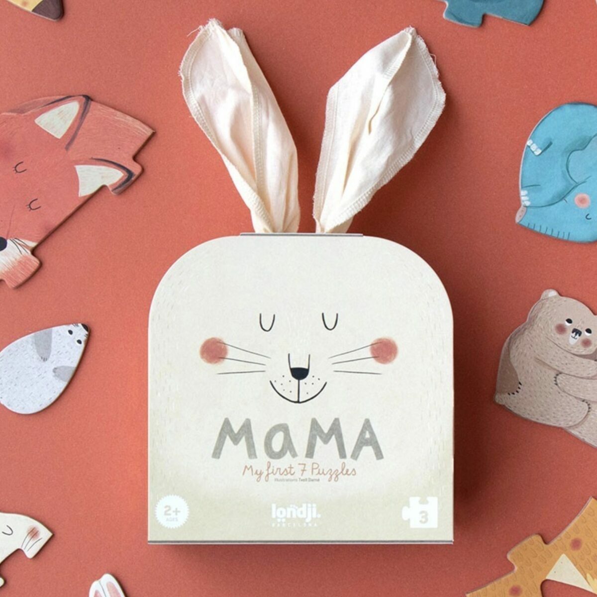 Boîte du puzzle Mama Londji présentée dans un sac en tissu blanc avec des oreilles de lapin qui dépassent et un visage de lapin imprimé.