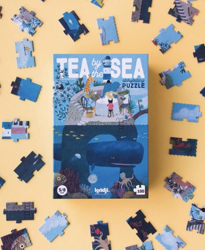 Boîte rectangulaire verticale du puzzle Londji Tea by the Sea illustrant des personnages prenant le thé au bord de l'eau.