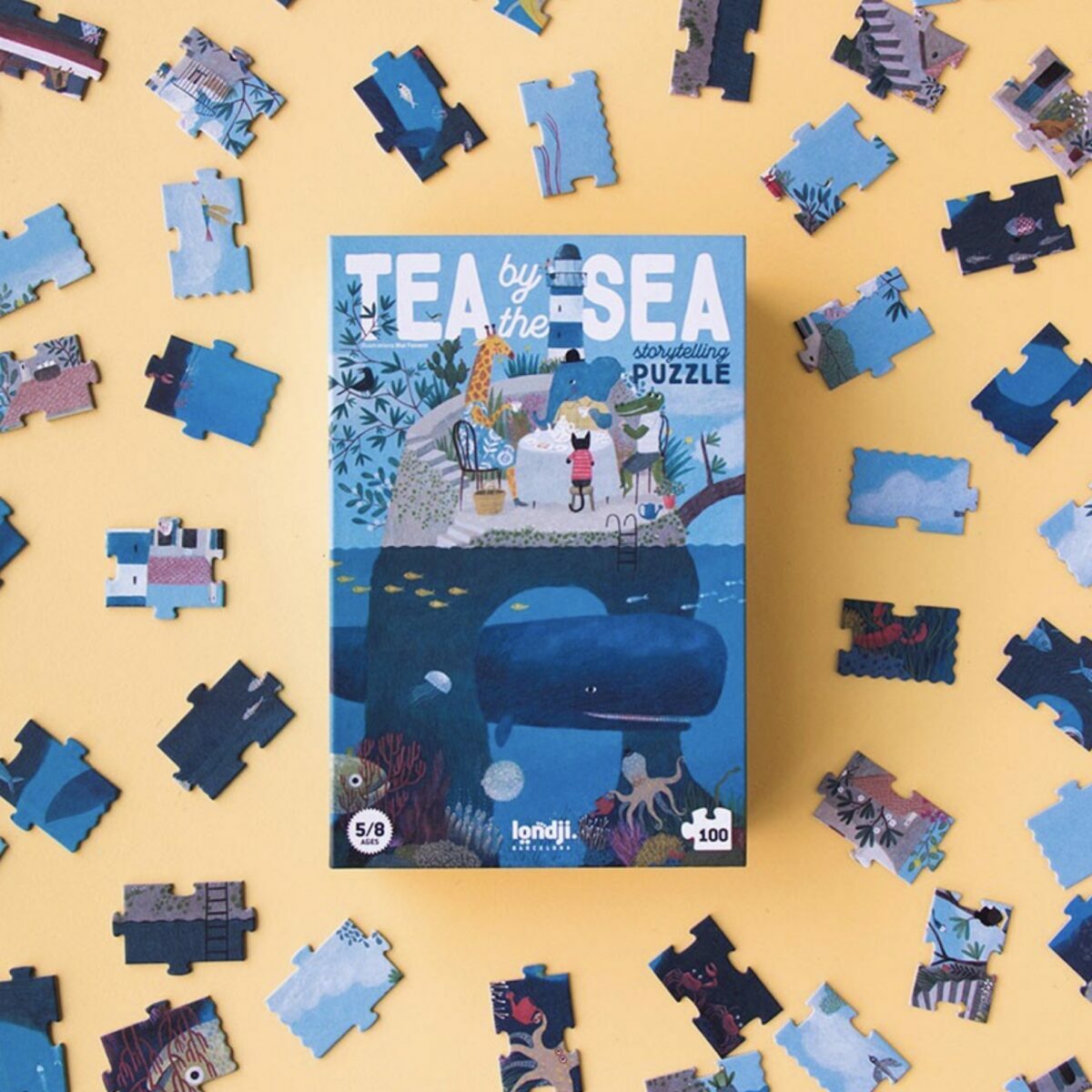 Boîte rectangulaire verticale du puzzle Londji Tea by the Sea illustrant des personnages prenant le thé au bord de l'eau.